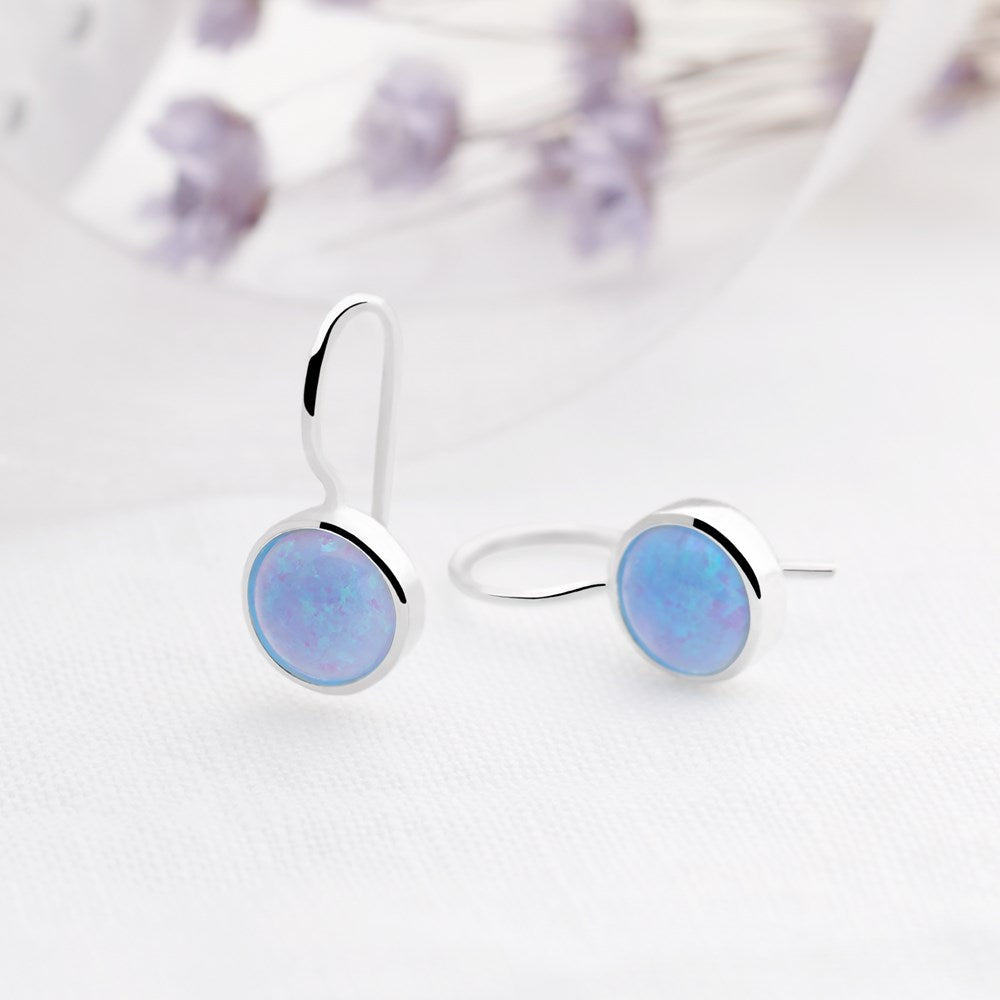 A pair of dainty silver drop earrings featuring round, bezel-set vibrant blue opal cabochons on wire hooks.
