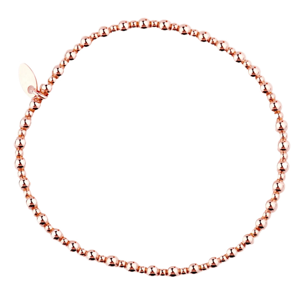 A rose gold-colored bracelet with beads, featuring a high polish finish and a small charm.