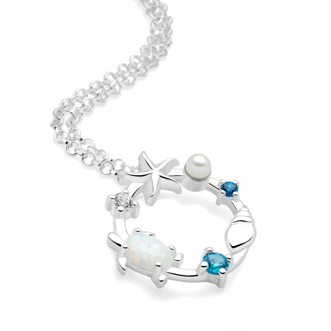 A silver necklace with a sea-themed design, featuring opals, a turtle, a shell, a starfish, a pearl, and sparkling cubic zirconia, displayed against a white background.