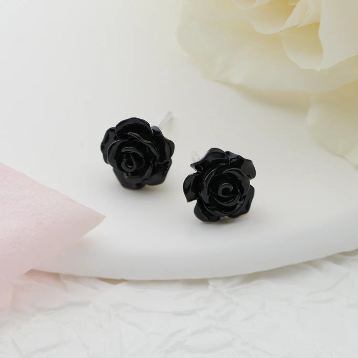 Black rose-shaped earrings on a white fabric background