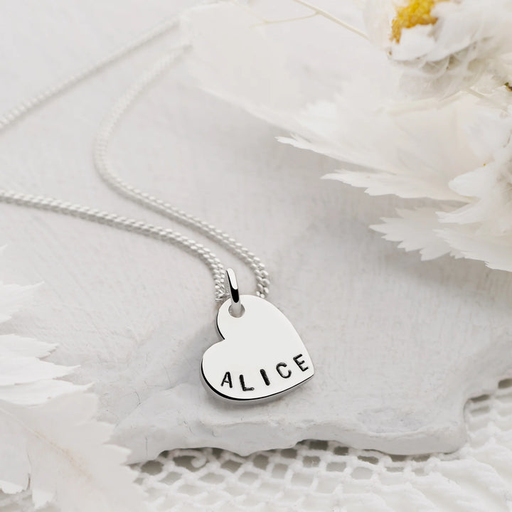 Silver necklace with a heart-shaped pendant engraved with 'ALICE' on a white floral background