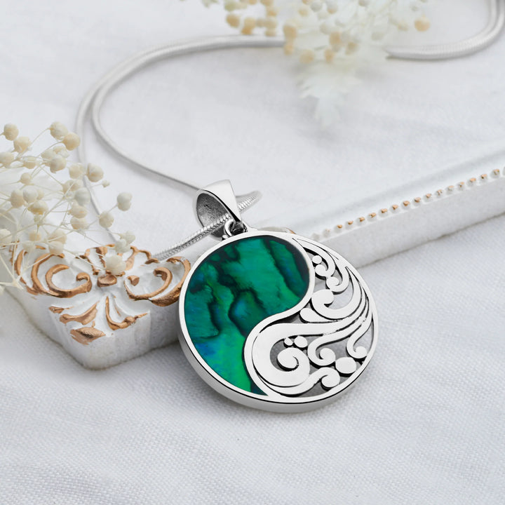 Silver necklace with a green and white pendant on a white surface with decorative elements.