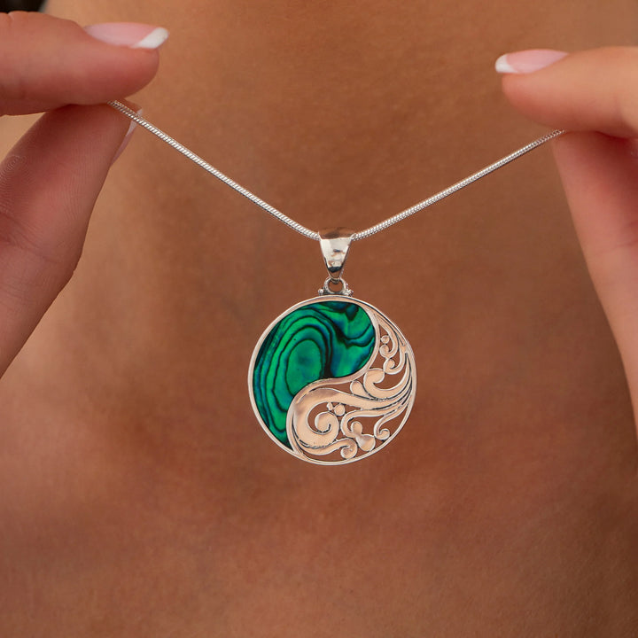 Necklace with a circular pendant featuring green and gold designs held by hands against a brown background