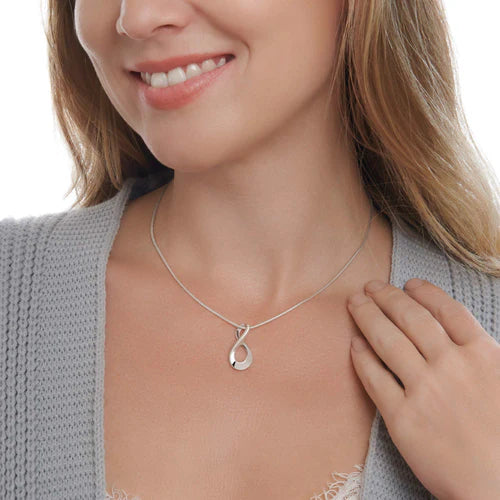 Woman wearing a silver necklace with a pendant on a plain background