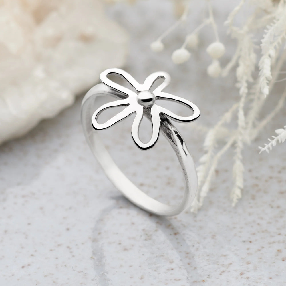 A silver ring with a daisy flower design on the top, featuring a high polish finish on the flower and a satin finish band. Neutral background. 