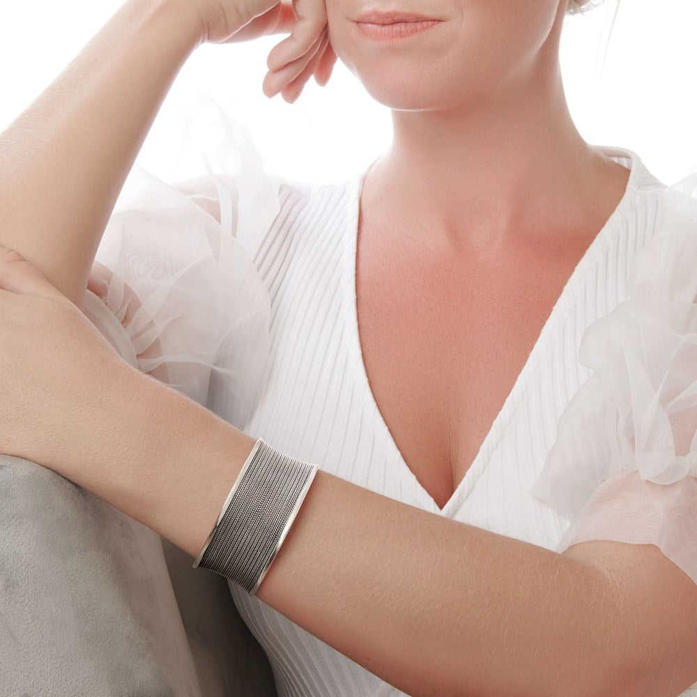 A silver bangle bracelet with intricate filigree wire work, displayed on female model.