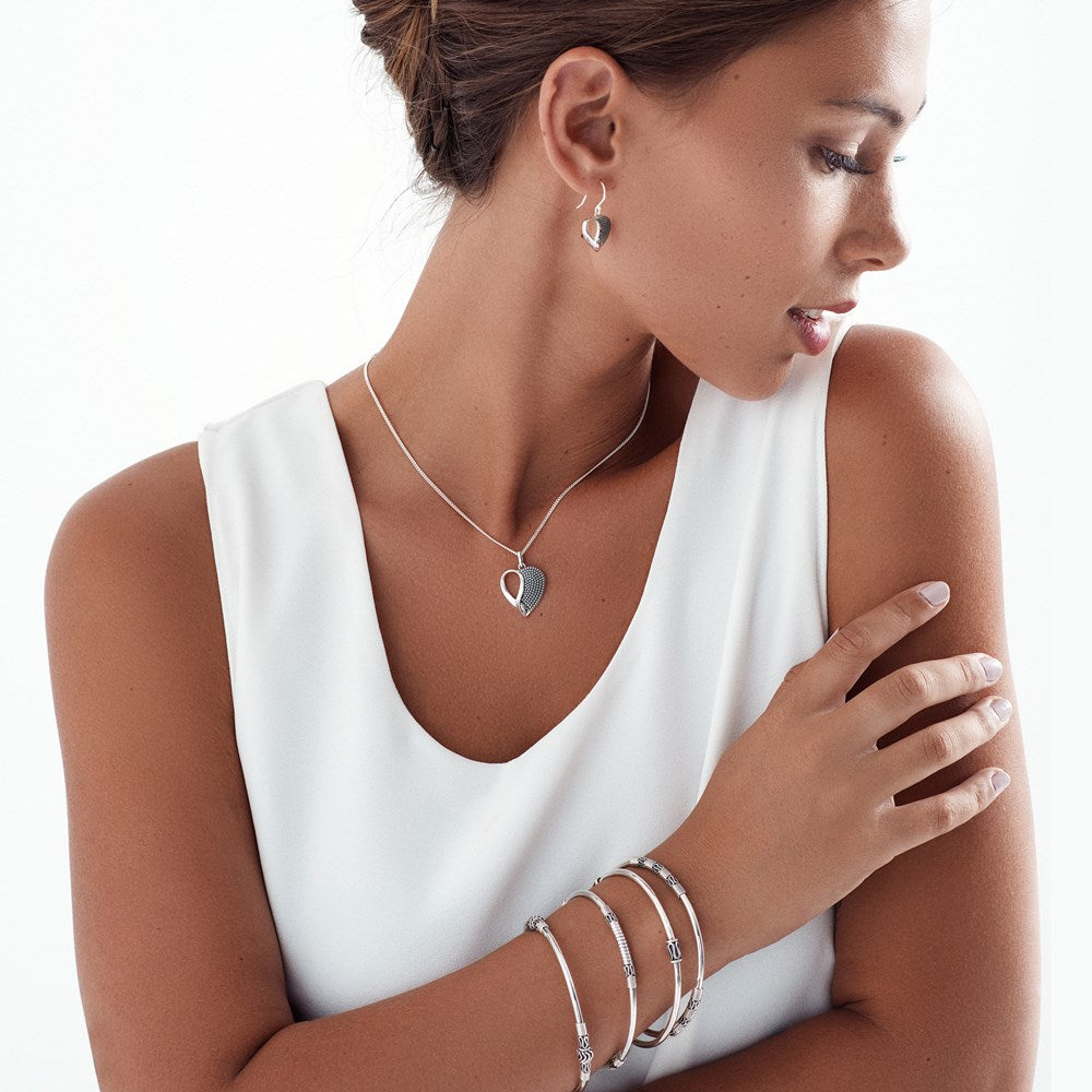 A sterling silver bangle with intricate Balinese scrollwork, featuring a high polish finish with oxidised details on female model