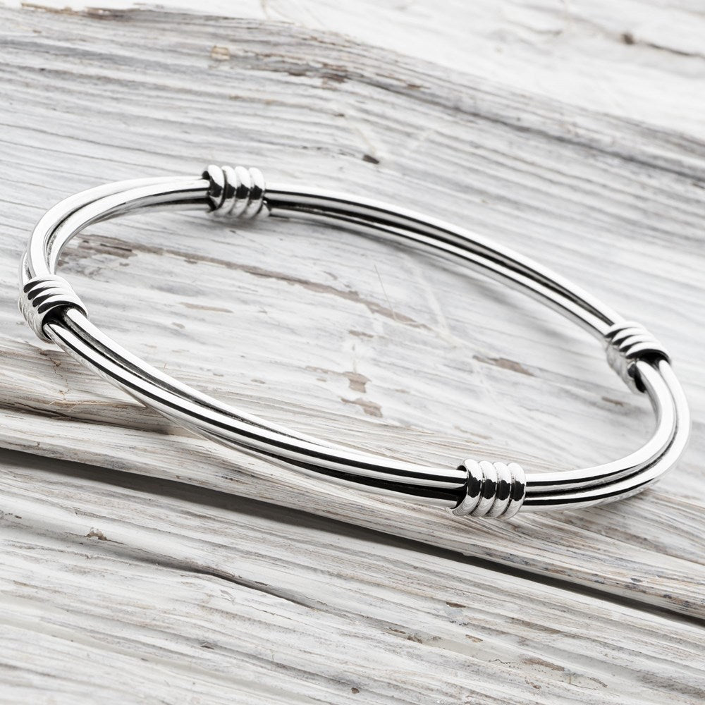 A silver bangle bracelet with a high polish finish, featuring a trio of interlinked loops held in place by four stylish links positioned north, south, east, and west.