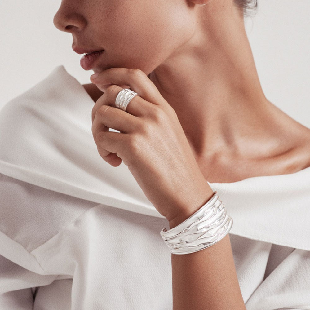 A person wearing a white shirt showcases a silver bangle bracelet with a high shine and satin finish.