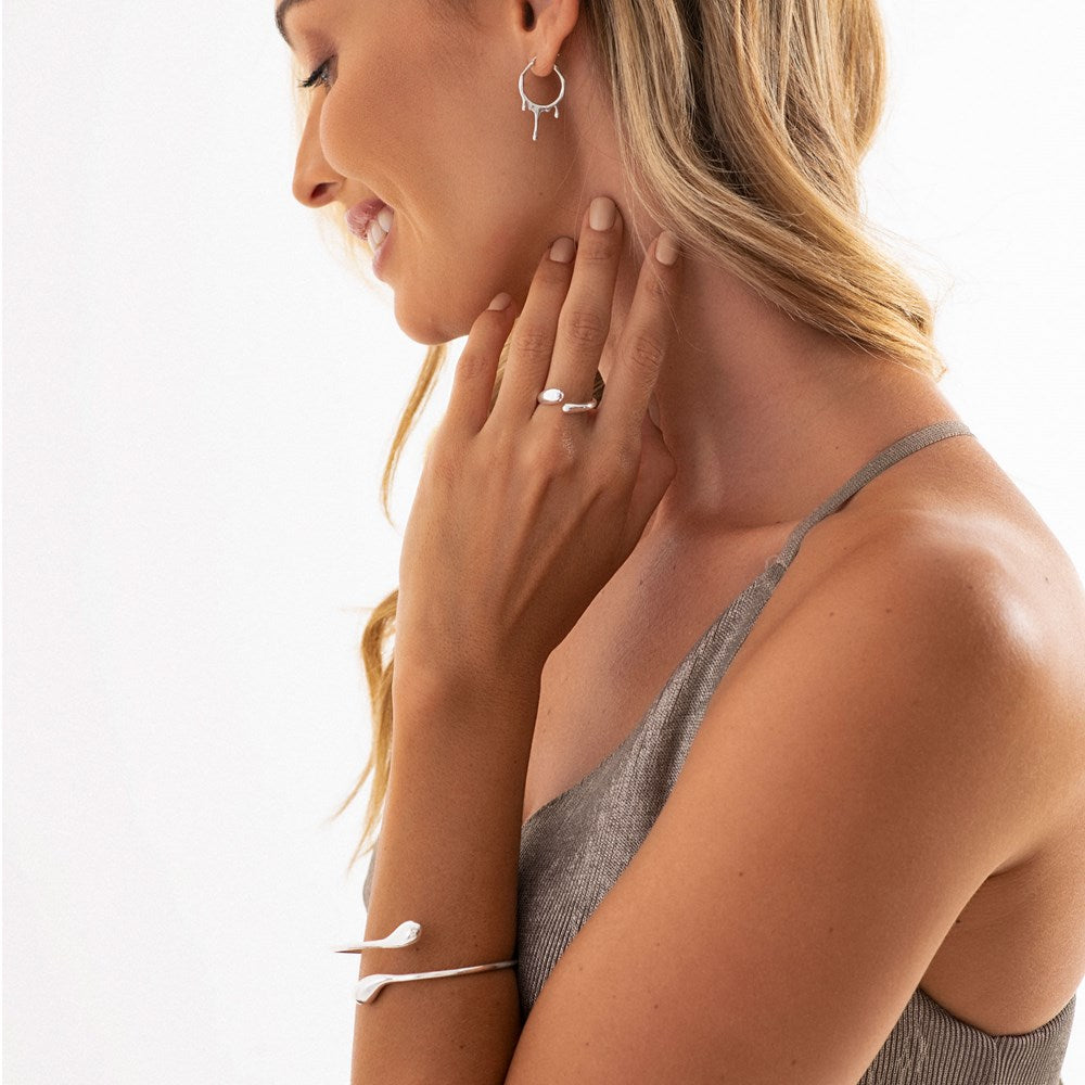 A silver bangle bracelet with a design that ends in two raindrop shapes, on woman model and ring. 