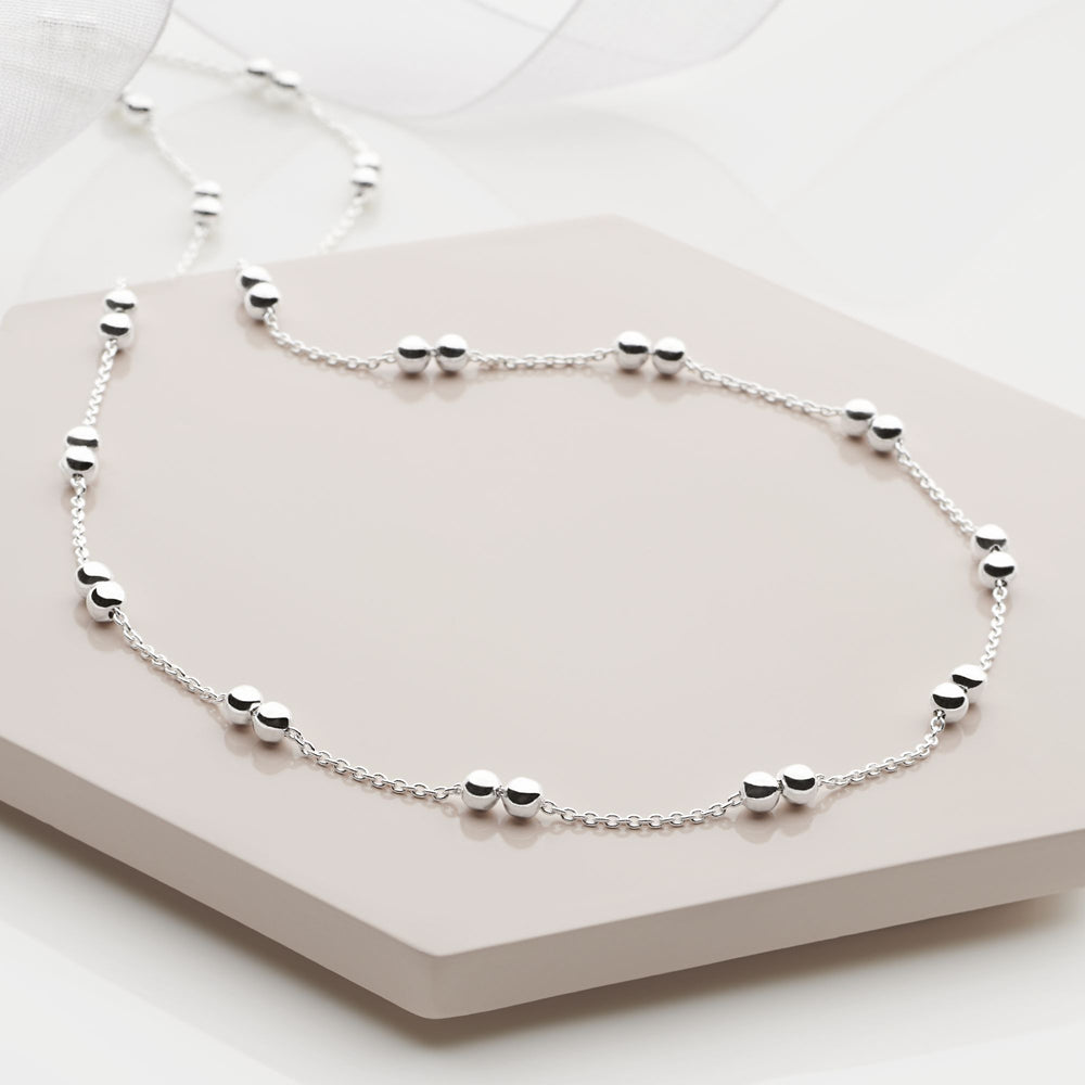 A silver necklace with beads threaded on a link chain, displayed on a white stand.
