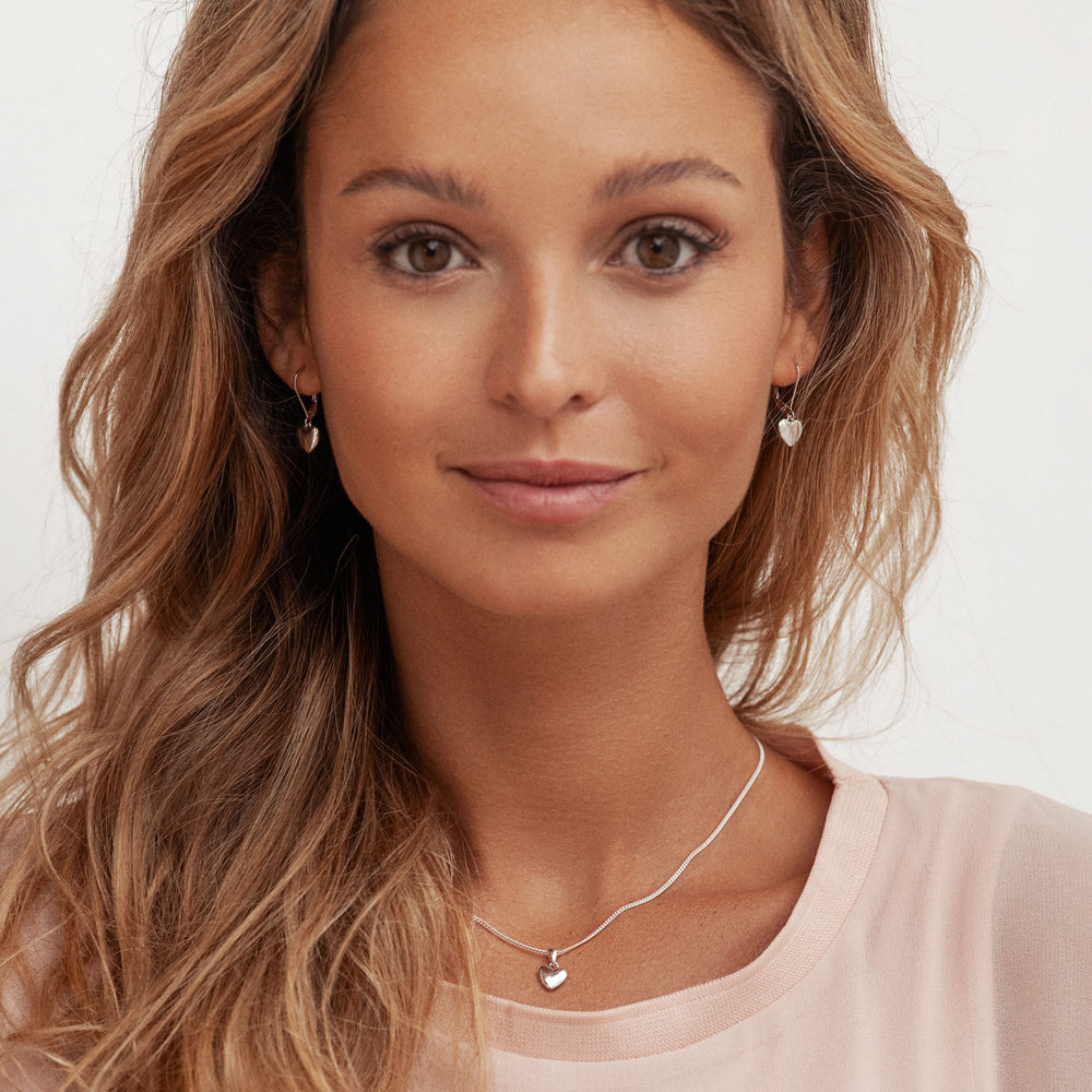 A pair of silver heart-shaped drop earrings with a high polish finish and secure clip fastening on model.