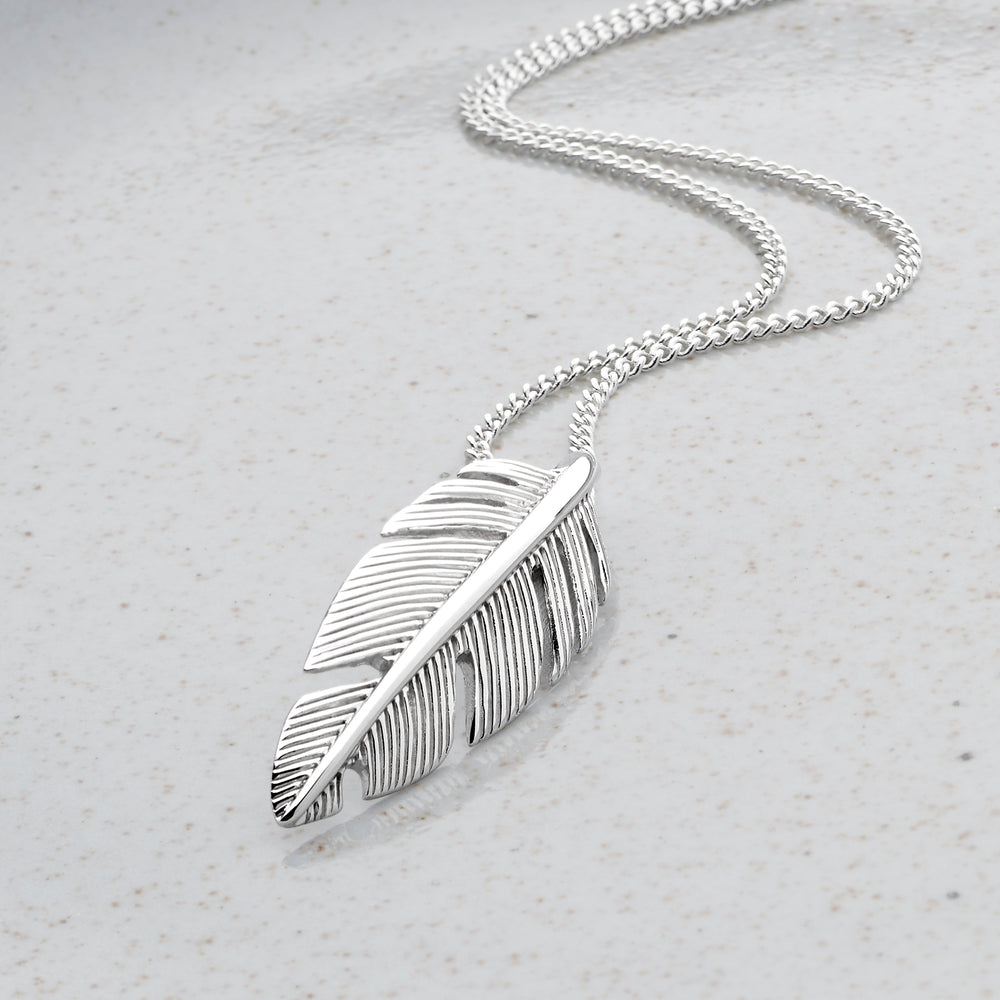 A 925 sterling silver feather pendant necklace with a curb chain on a textured background.