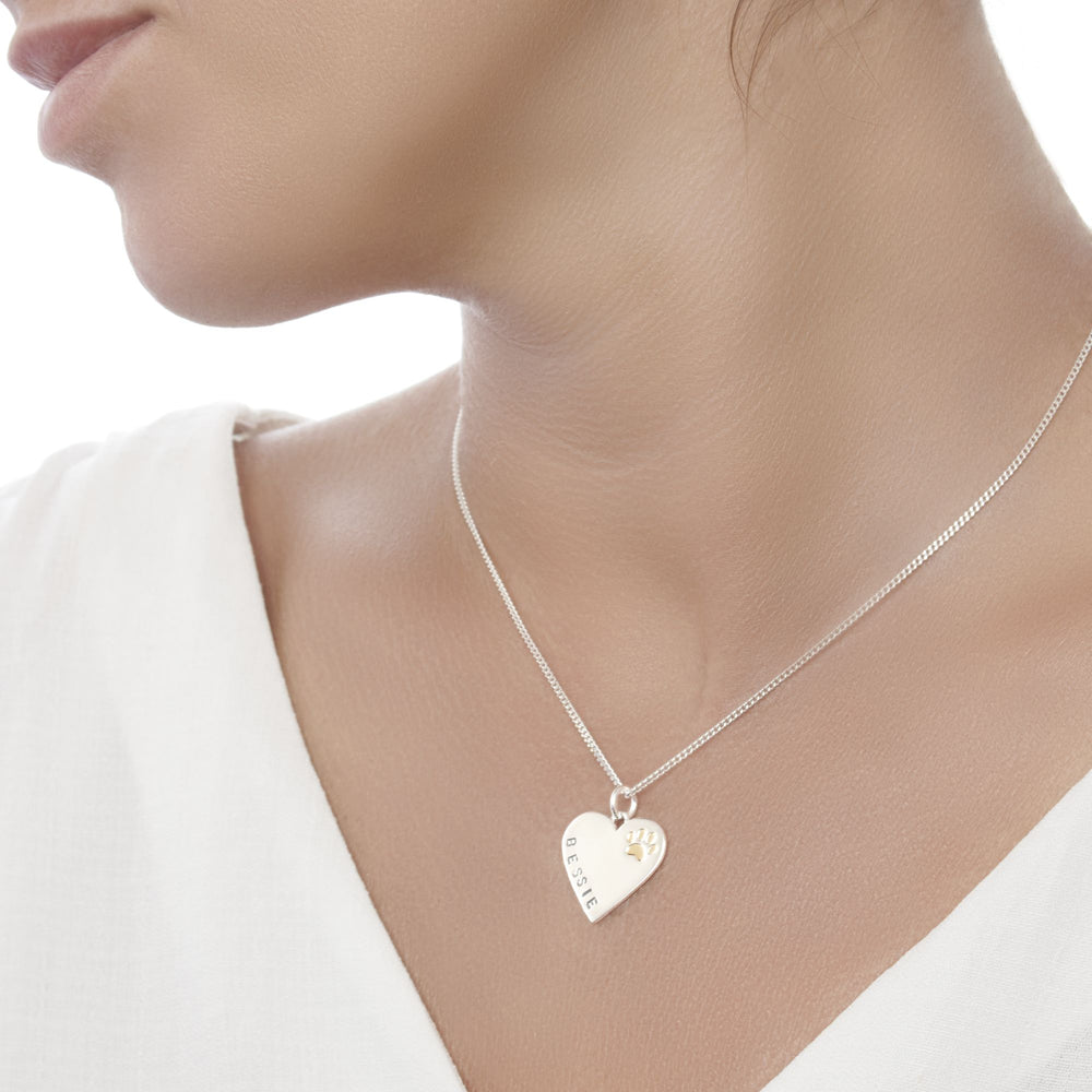 A silver pendant in the shape of a heart with a paw print and the name 'BESSIE' stamped on it, attached to a 40cm curb chain.