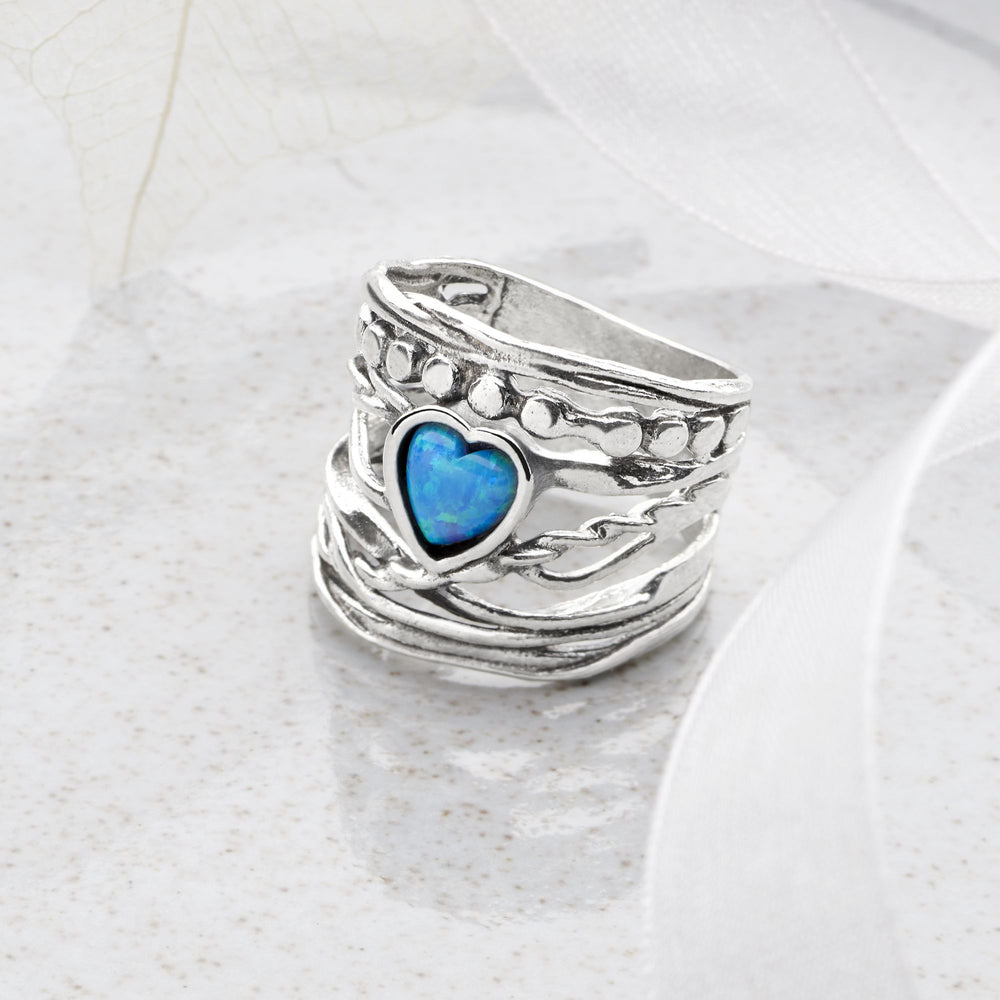 A sterling silver ring with a blue opal heart-shaped design at the center, surrounded by a woven pattern.